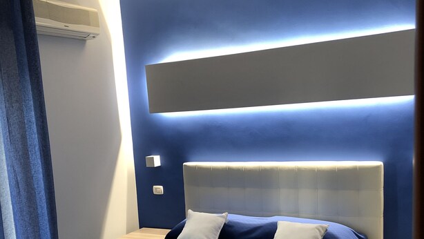 Une chambre d’hôtel moderne, dotée d’un grand lit, d’une table de chevet, d’une petite table et d’un climatiseur fixé au mur.