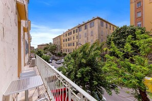 A balcony with a metal table and red carpet, overlooking a street with cars and buildings.