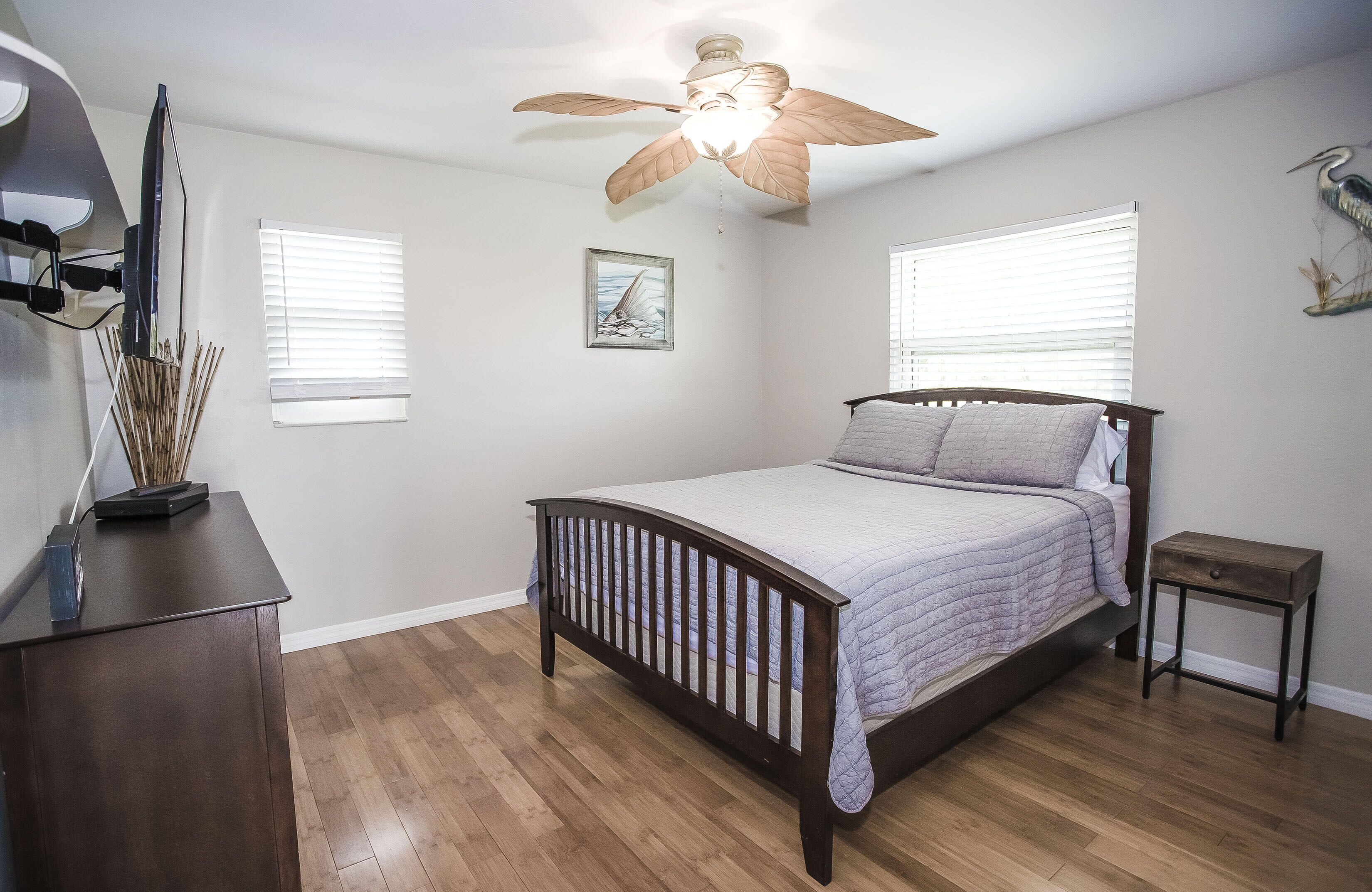 A bedroom with a wooden bed, a ceiling fan, and two windows with blinds.