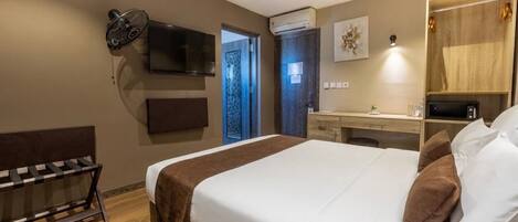 A hotel room with a bed, a desk, a TV, and an air conditioning unit.