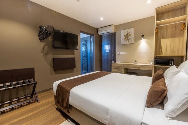 A hotel room with a bed, a desk, a TV, and an air conditioning unit.