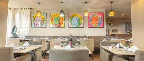 L’intérieur d’un restaurant, avec des banquettes, des tables et des œuvres d’art accrochées aux murs.