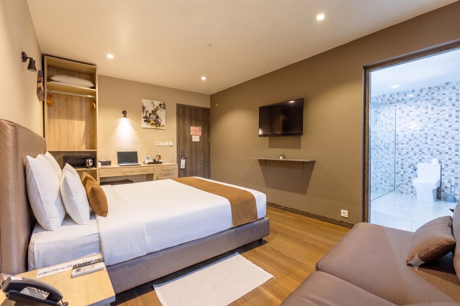 A modern hotel room with a bed, a desk, a TV, and a bathroom visible through a glass door.
