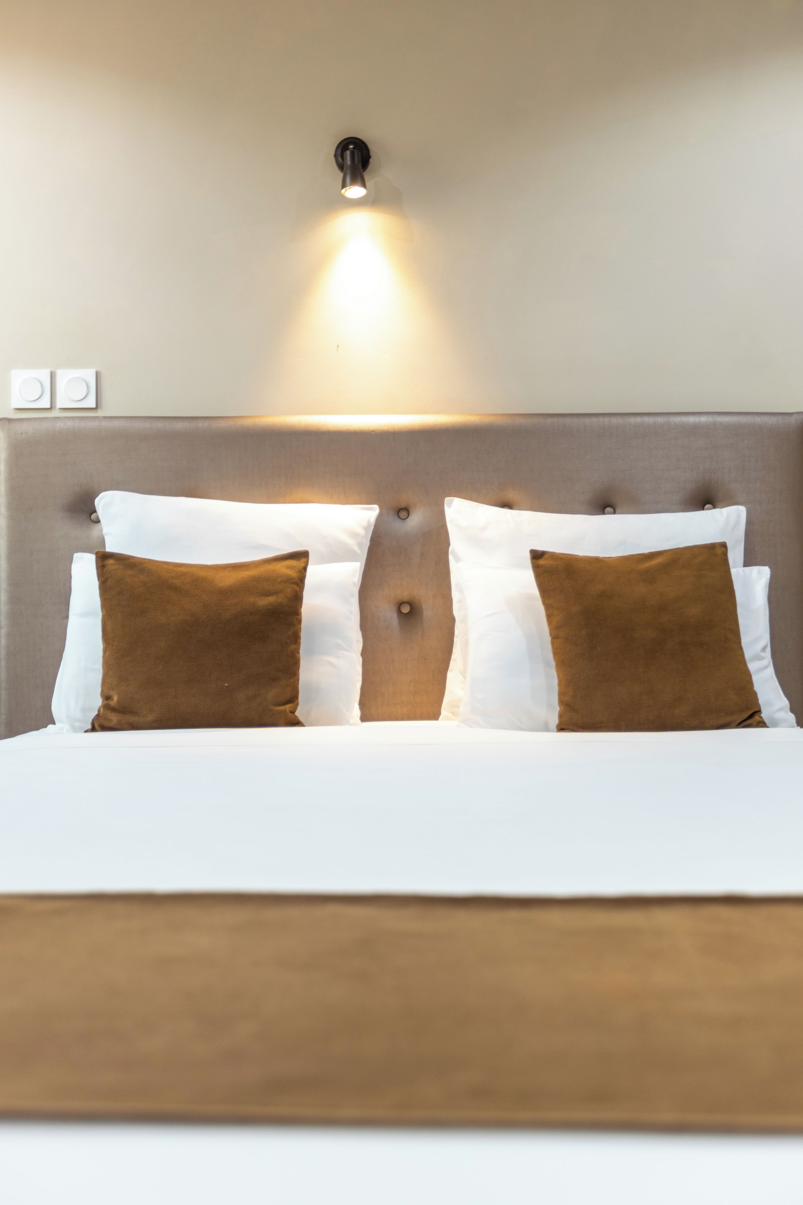 A bed with a headboard, two white pillows, and two brown pillows.