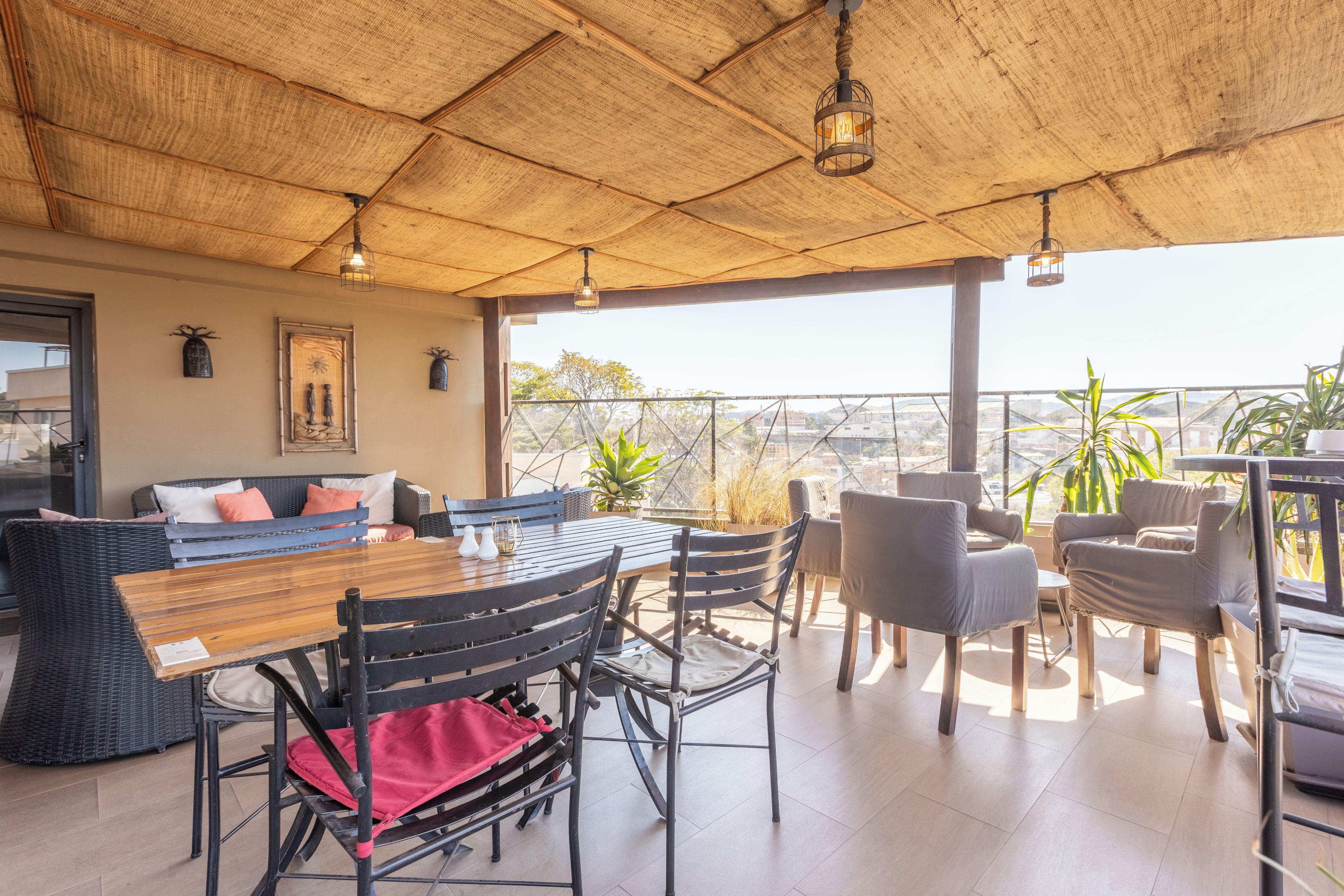 A spacious outdoor seating area with a wooden table and chairs, a wicker sofa, and a view of the cityscape.