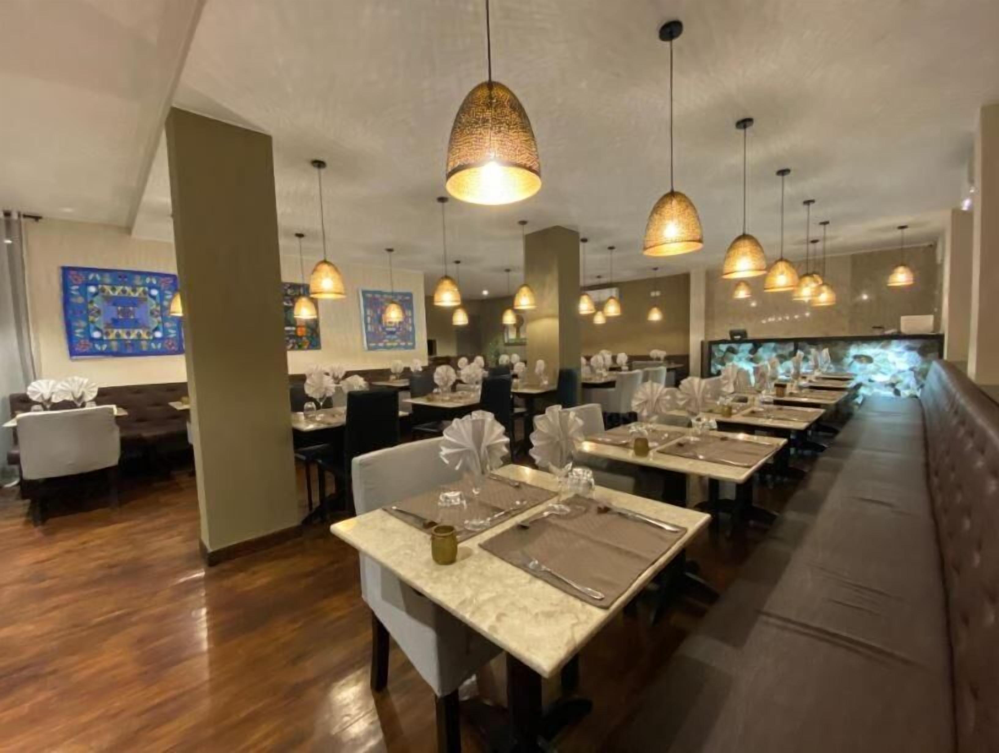 A restaurant with multiple dining tables, hanging pendant lights, and a long bench along the wall.