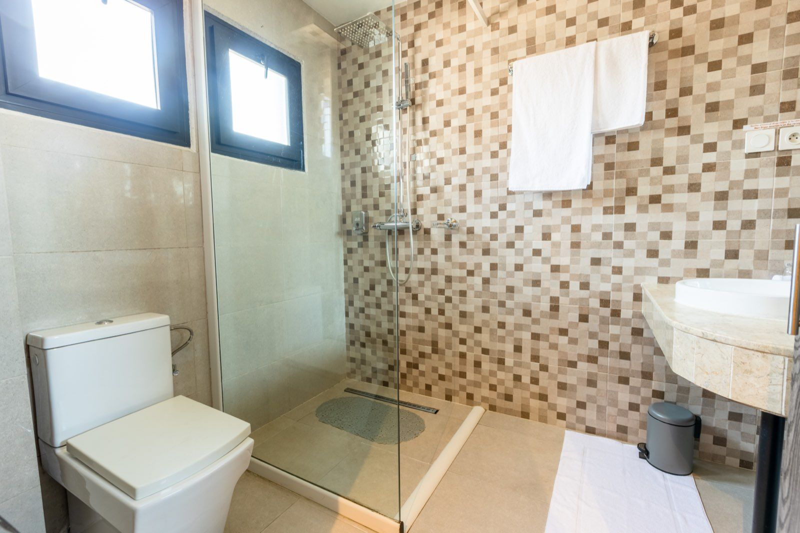 Un baño con ducha de vidrio, inodoro, lavamanos y pared con azulejos.