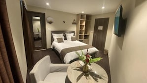 Une chambre d’hôtel avec un lit, une chaise, une petite table sur laquelle se trouve un vase, et un téléviseur fixé au mur.