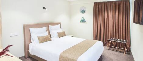 Quarto de hotel bem arrumado com uma cama grande, uma mesa de cabeceira e um pequeno espaço de estar com uma cadeira e uma mesa.
