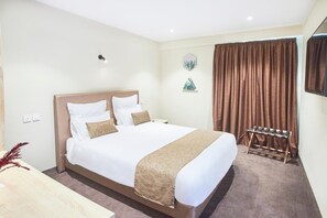 A neatly arranged hotel room with a large bed, a bedside table, and a small seating area with a chair and a table. - Fly Inn Madagascar Hotel (Antananarivo)