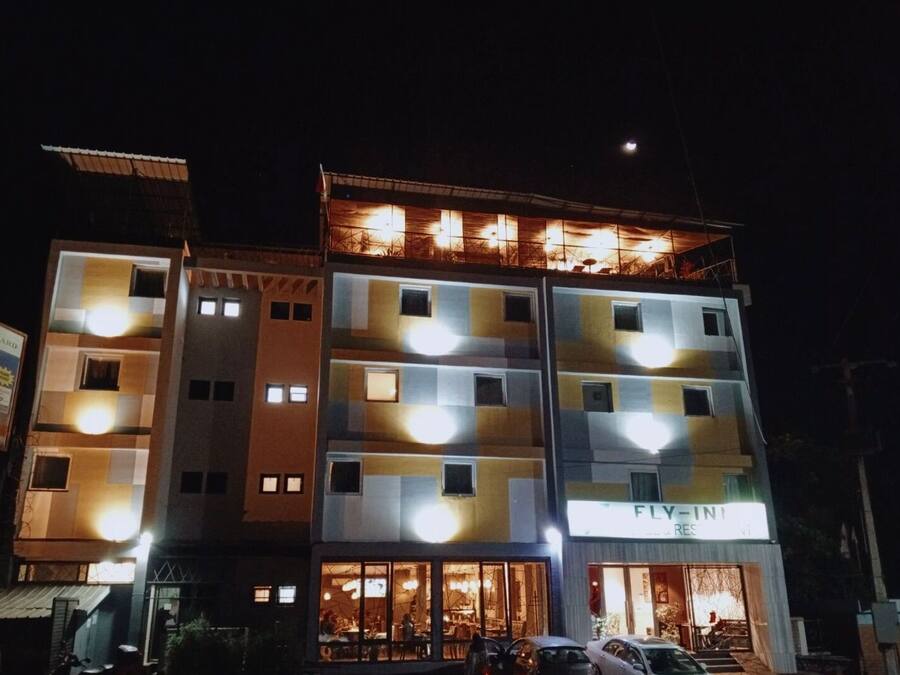 Un edificio de varios pisos con ventanas iluminadas y un restaurante llamado "FLY-IN" en la planta baja.
