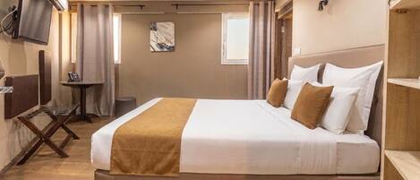 A hotel room with a large bed, a flat-screen TV mounted on the wall, a small table, and a window with curtains.