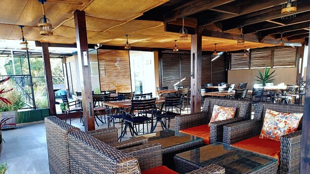 Un espace extérieur aménagé, abrité et doté de mobilier en osier et de tables, offrant une vue sur la verdure environnante.