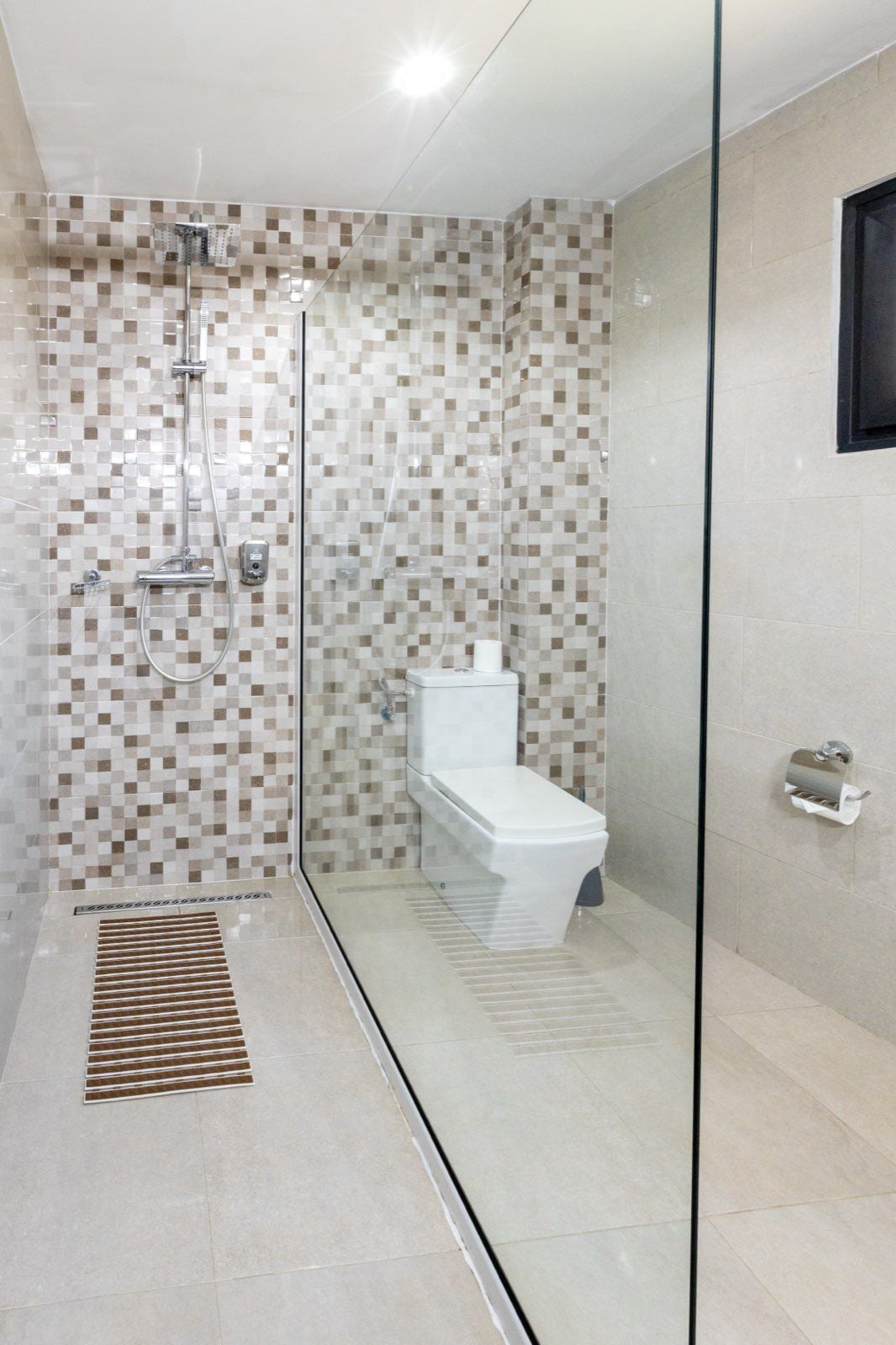 A modern bathroom with a glass shower enclosure, a toilet, and a hand dryer.