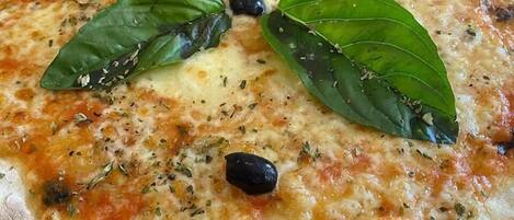 Pizza com folhas de manjericão e azeitonas pretas por cima.