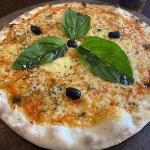 A pizza with basil leaves and black olives on top. - Fly Inn Madagascar Hotel (Antananarivo)