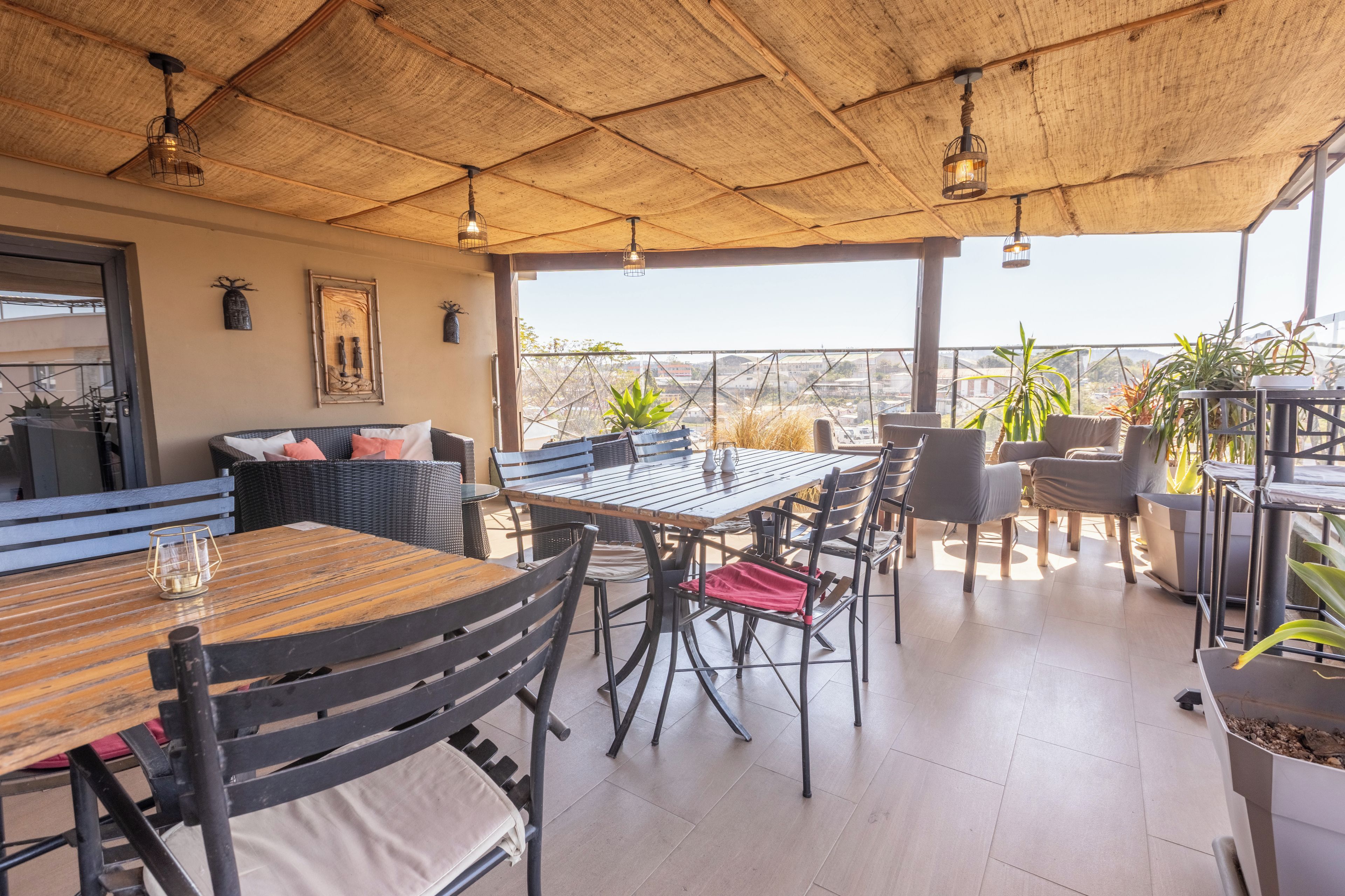 An outdoor patio with a wooden table and chairs, surrounded by potted plants and a view of the cityscape.