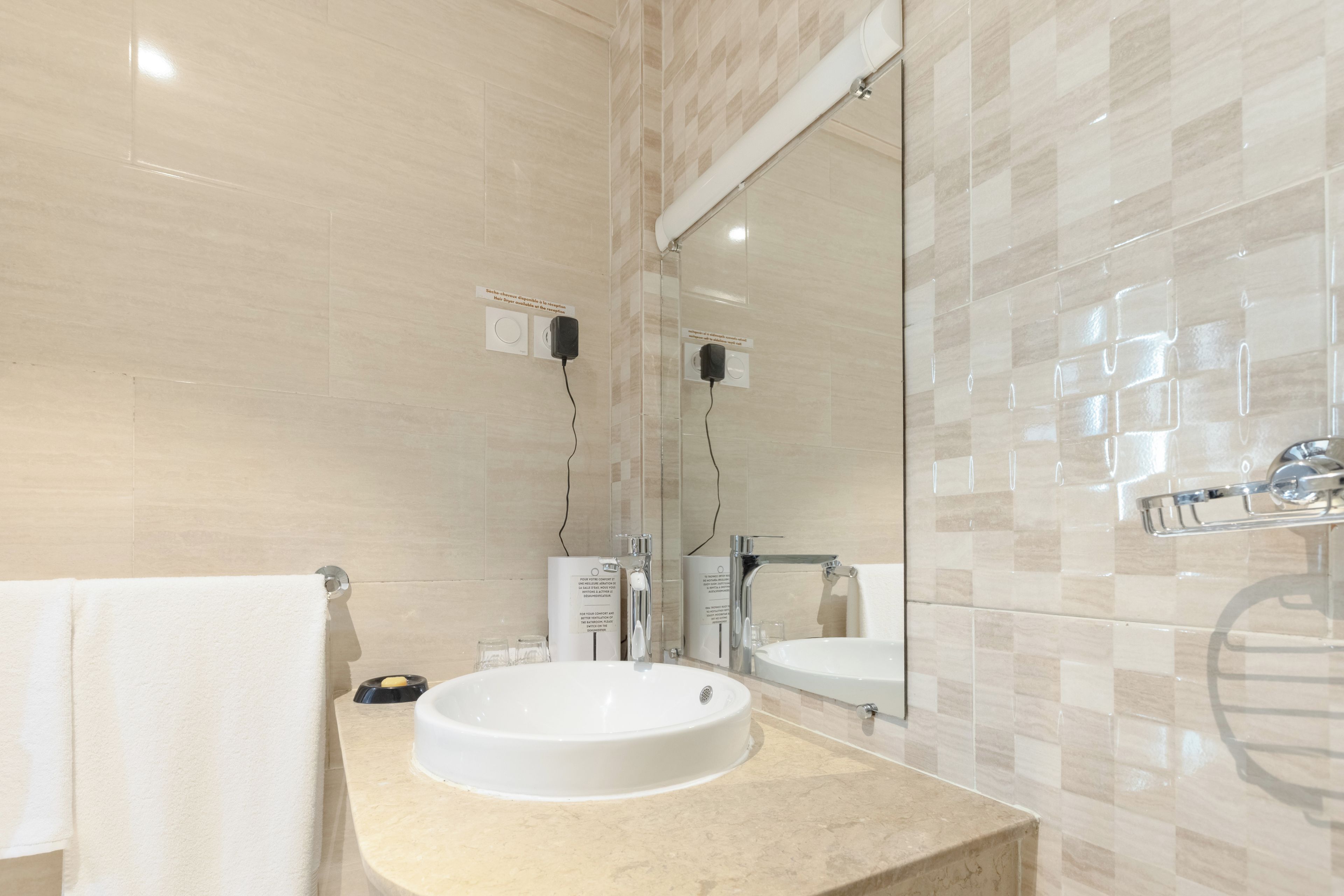 Un baño con un lavamanos blanco, un espejo y un perchero para toallas.