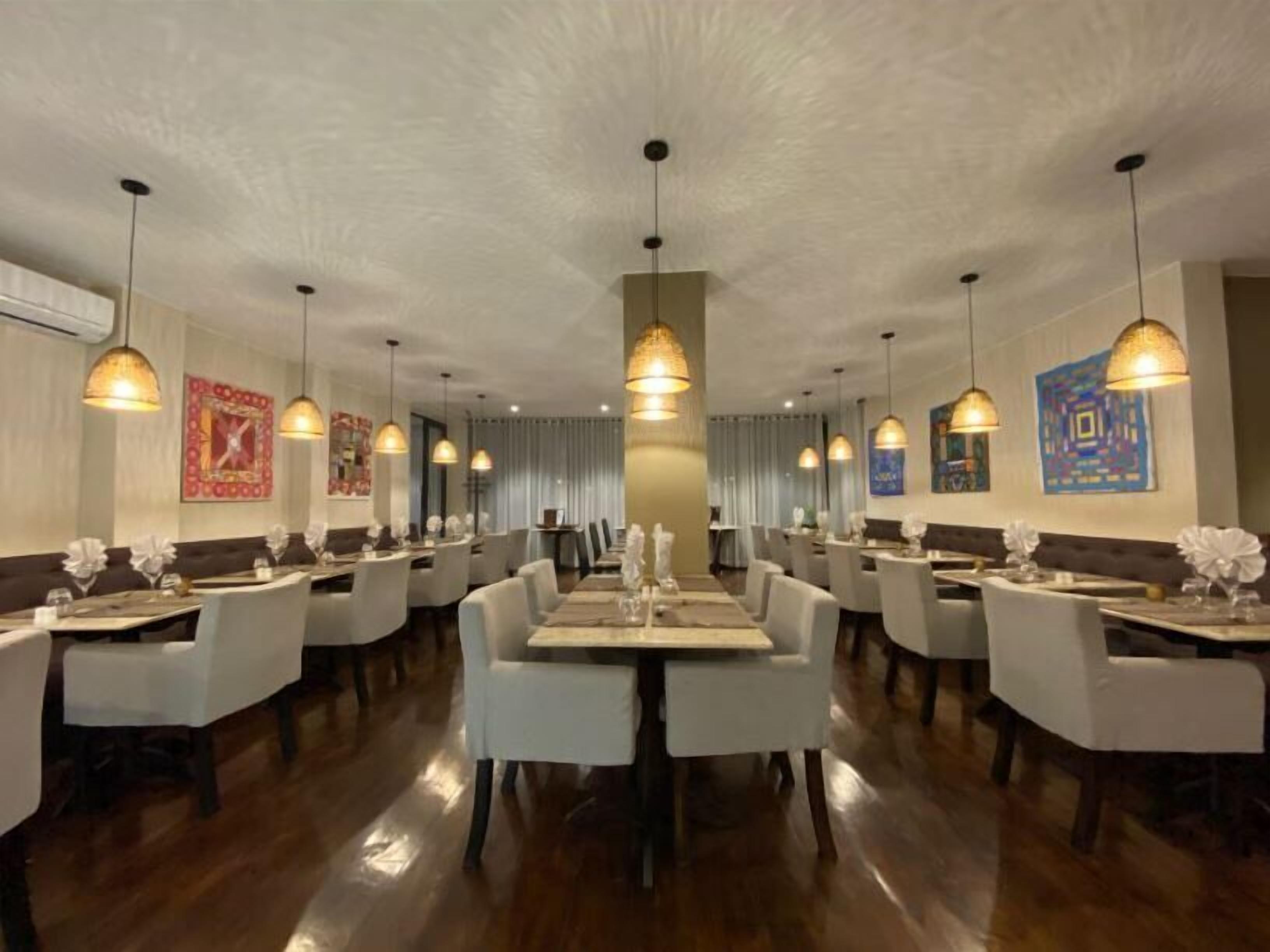 A restaurant with multiple dining tables and chairs, pendant lighting, and artwork on the walls.