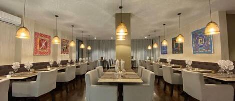 A restaurant with multiple dining tables and chairs, pendant lighting, and artwork on the walls.