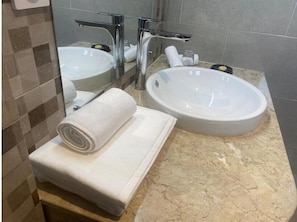A bathroom with two sinks, a mirror, and a towel on a shelf. - Fly Inn Madagascar Hotel (Antananarivo)