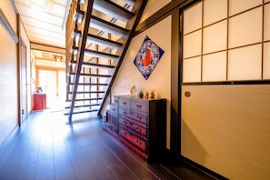 Traditional Japanese interior with a wooden floor and sliding doors, featuring a staircase and decorative wall hanging.