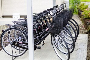 Een rij fietsen geparkeerd in een open gebied met een betonnen pad en een gebouw op de achtergrond.