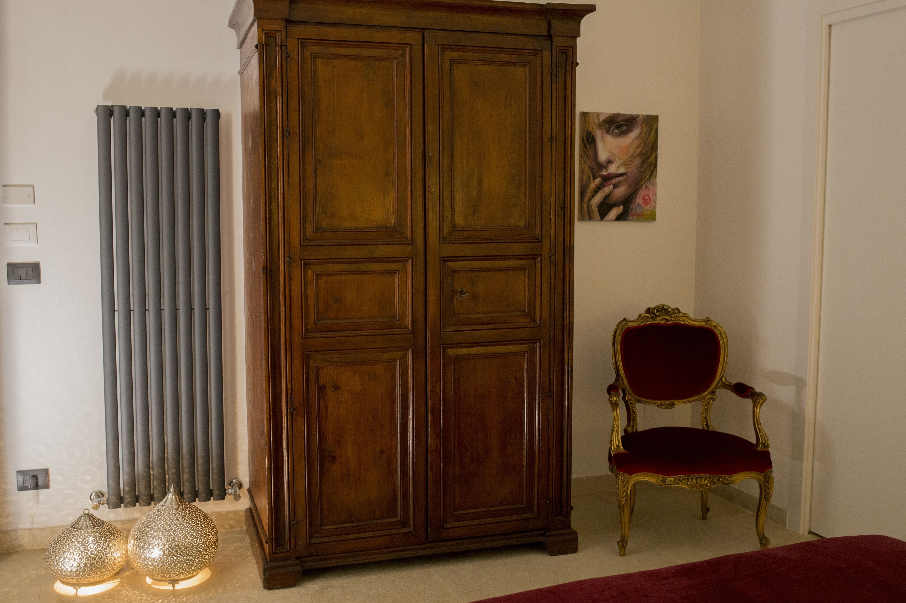A room with a large wooden wardrobe, a radiator, a chair, and two decorative lamps.