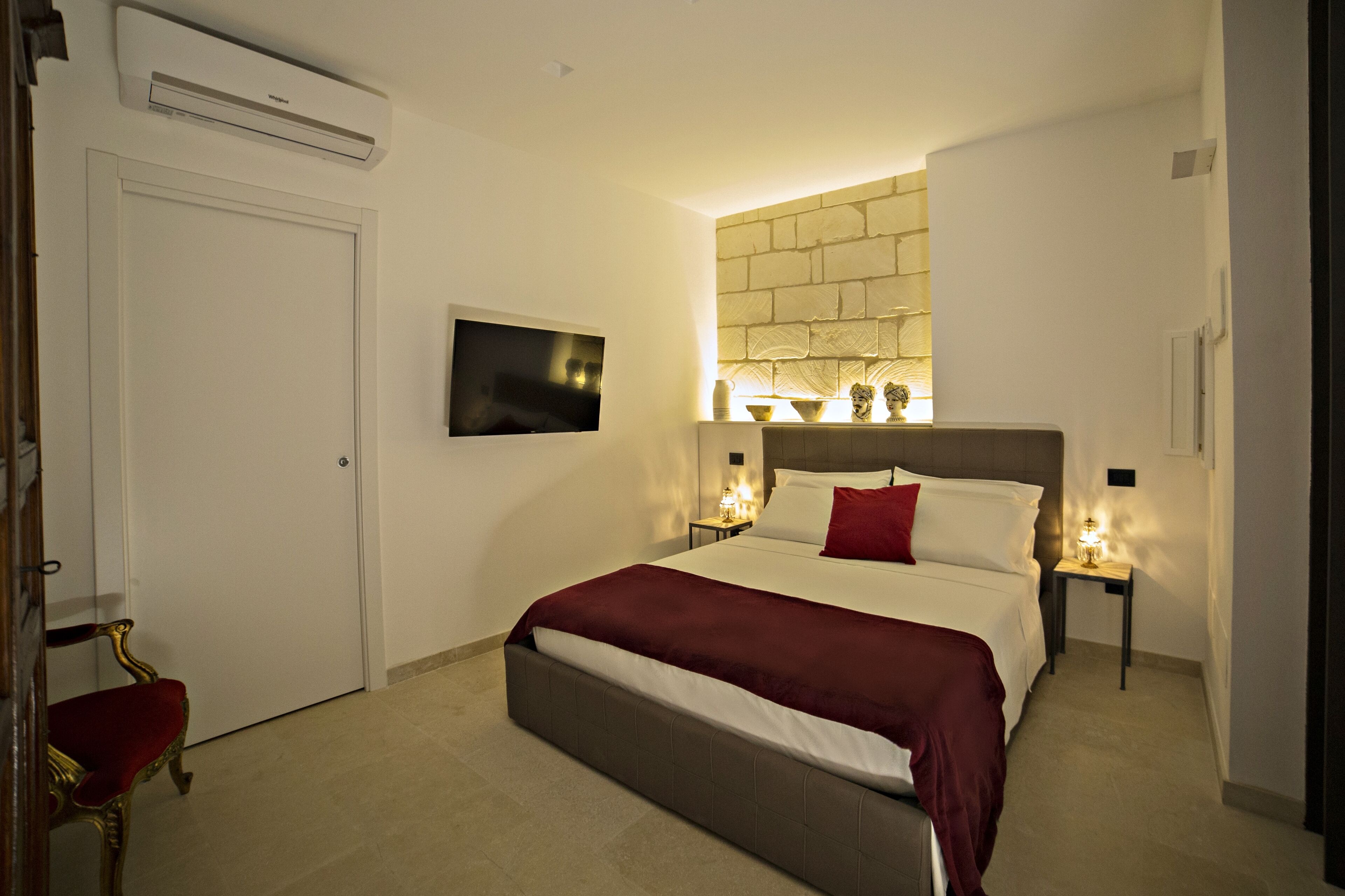 Ein Hotelzimmer mit Bett, Fernseher, Wandairconditioner und einem kleinen Tisch mit Lampe.