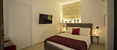 Una habitación de hotel con cama, televisión, aire acondicionado instalado en la pared y una pequeña mesa con lámpara.