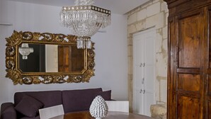 Een eethoek met een ronde houten tafel, een witte vaas, een donkere bank, een grote versierde spiegel en een houten kast.