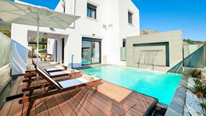 A modern house with a swimming pool, wooden deck, and lounge chairs.