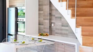 A modern kitchen with a built-in oven, a dining area with a white table and metal chairs, and a staircase with wooden steps.
