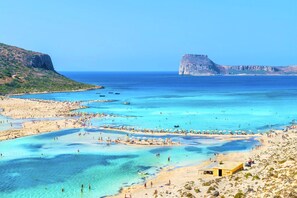 A coastal beach scene with clear blue waters, sandy shores, and rocky cliffs.
