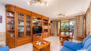 Een woonkamer met een televisie, houten kasten, een salontafel en blauwe banken.