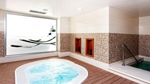 A modern spa area with a hot tub, wooden flooring, and a mosaic wall.