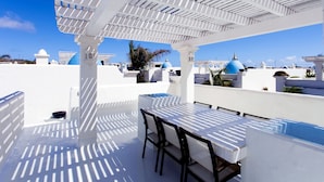 A rooftop terrace with a white pergola, a table with chairs, and a view of blue-domed buildings.