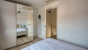 Une chambre à coucher comprenant un lit, une armoire, un miroir, une planche à repasser et une porte donnant sur un escalier.
