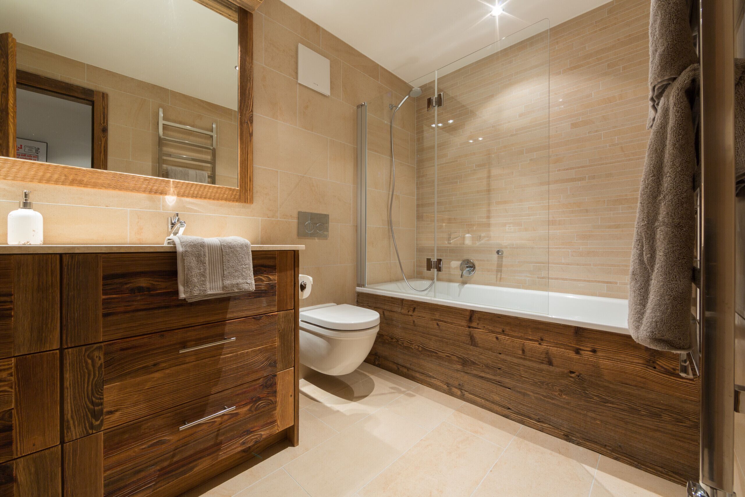 A modern bathroom with a wooden vanity, a toilet, a bathtub, and a glass shower enclosure.