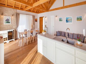 A modern kitchen with white cabinetry, a wooden dining table, and a striped sofa. - Villa Doline (Konavle)