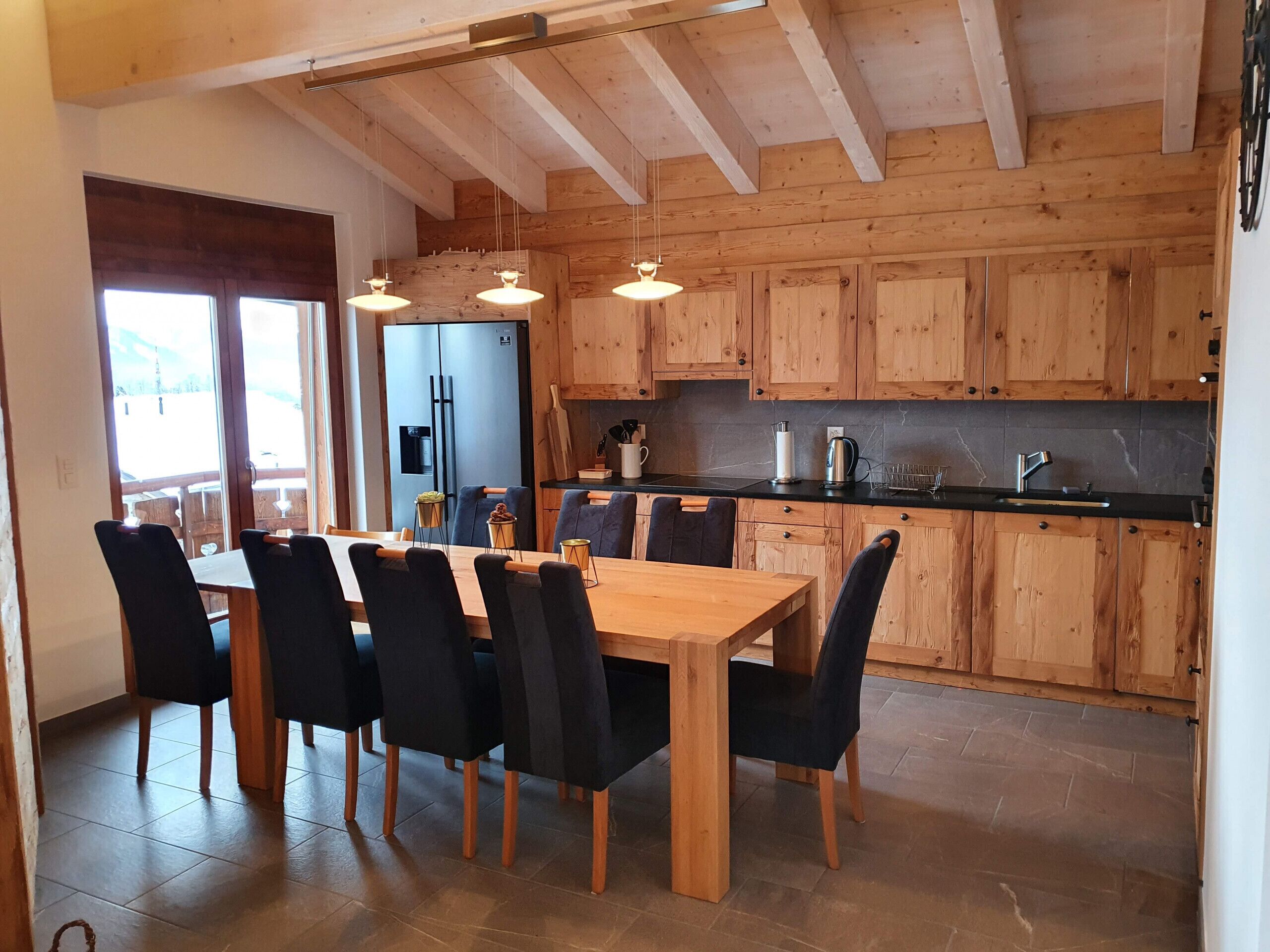 Une cuisine moderne avec des meubles en bois, un plan de travail noir et un coin repas comprenant une table et des chaises en bois.