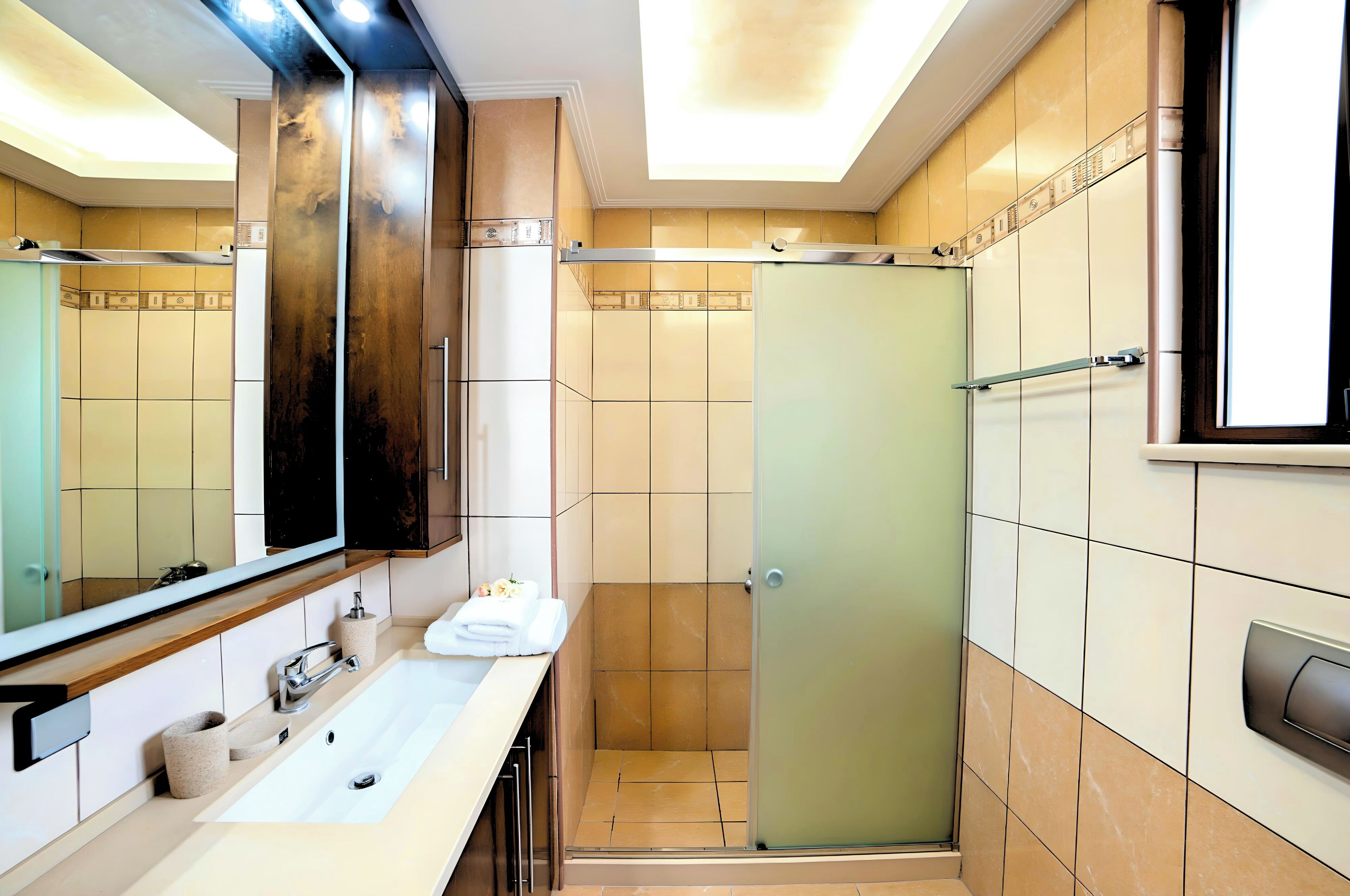 Un baño moderno con un espejo grande, un lavabo, una ducha y un inodoro.