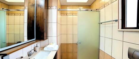 Un baño moderno con un espejo grande, un lavabo, una ducha y un inodoro.