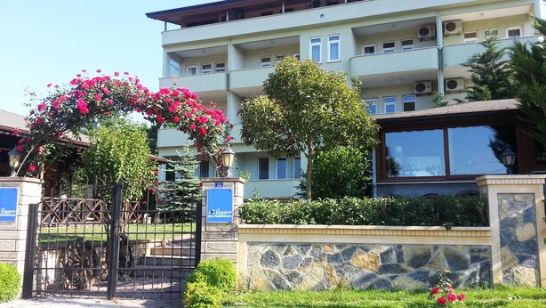 A multi-story building with a stone facade, a gated entrance, and a well-maintained garden with flowering plants. - Saygin Otel (Kandira)