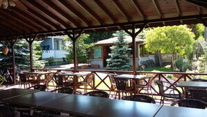 An outdoor patio area with tables and chairs, a covered roof, and a view of a building with a sign that reads "Sage." - Saygin Otel (Kandira)