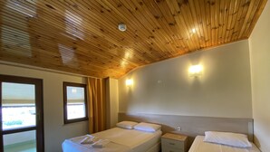 A room with two beds, a window with blinds, a wooden ceiling, and a wall-mounted light fixture. - Saygin Otel (Kandira)