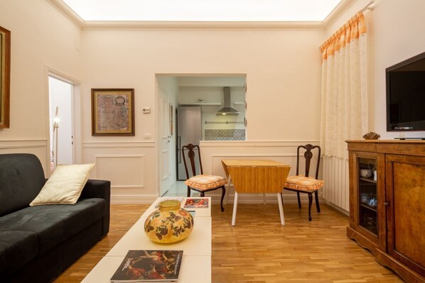 A living room with a sofa, a coffee table with a vase, two chairs, a wooden cabinet, and a television. - Casa Sole, an elegant apartment for rent in Florence by Mmega (Firenze)