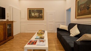 Un salon avec une table basse blanche, un canapé noir et des tableaux accrochés aux murs.