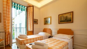 Une chambre d’hôtel avec deux lits, une fenêtre avec des rideaux, un tableau au mur et une vue sur le balcon extérieur.