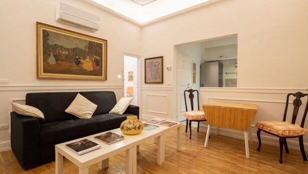 Un salon avec un canapé noir, une table basse blanche et une table d’appoint en bois.